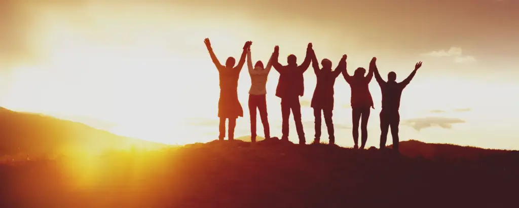 Gruppe von Menschen hebt im Sonnenuntergang gemeinsam die Arme – Symbol für Gemeinschaft und Zusammenhalt