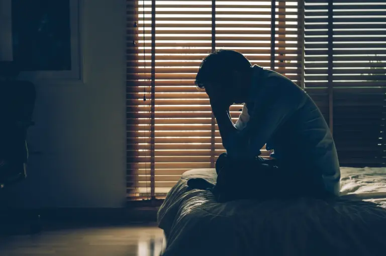Mann sitzt nachdenklich im dunklen Zimmer am Bett