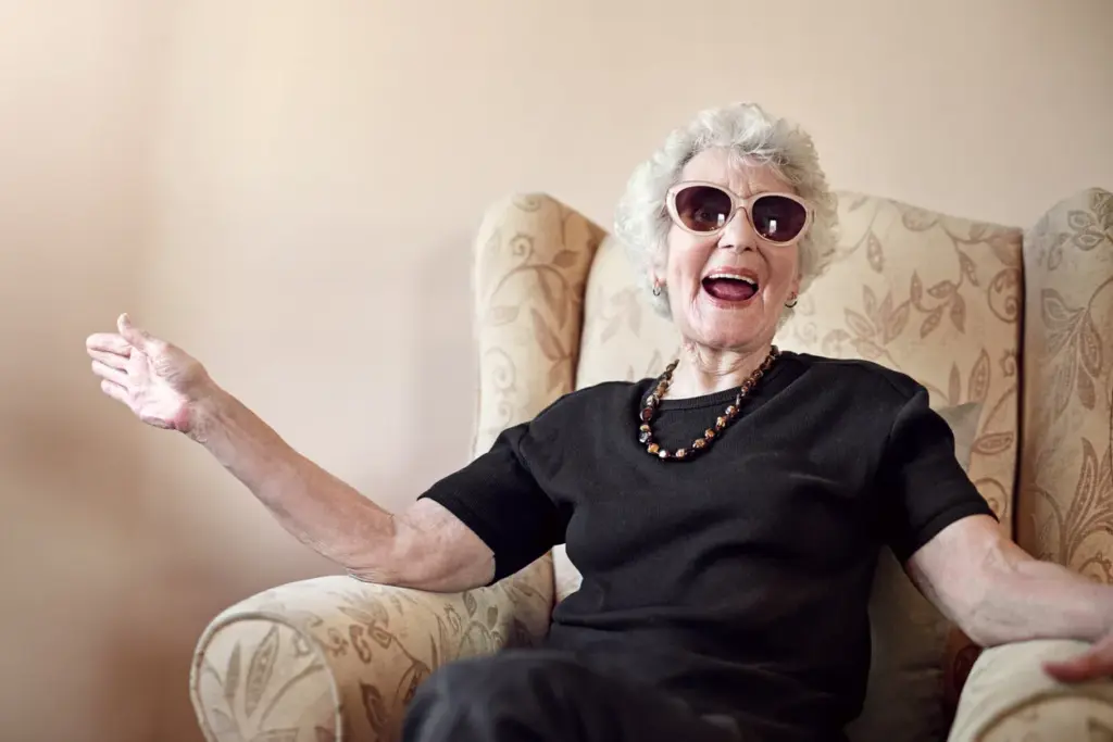 Fröhliche Seniorin mit Sonnenbrille sitzt entspannt im Sessel