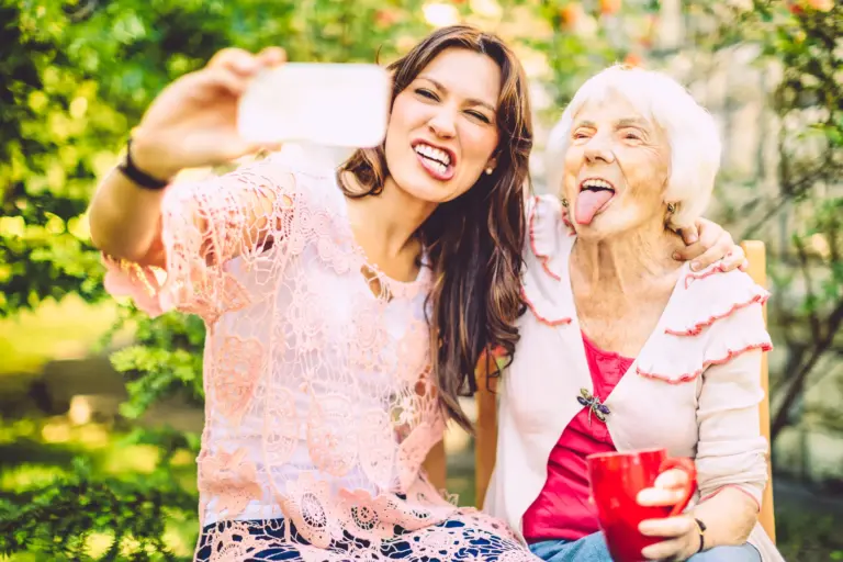 Junge Frau macht ein Selfie mit einer lachenden Seniorin im Garten
